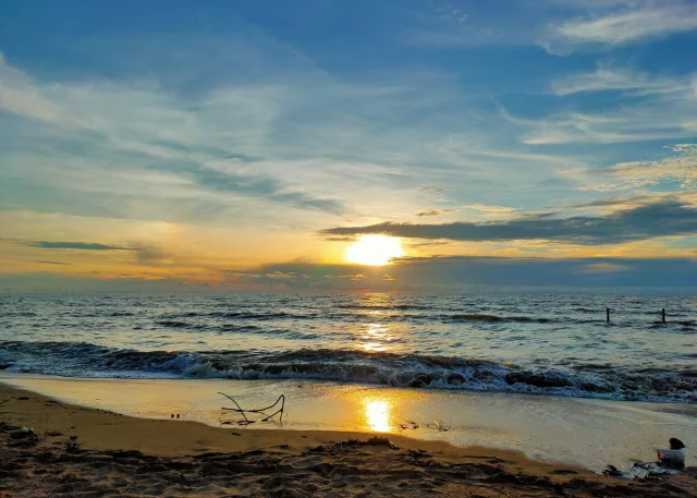 Matahari terbenam di atas laut, ombak kecil memecah di tepi pantai berpasir Pantai Batakan